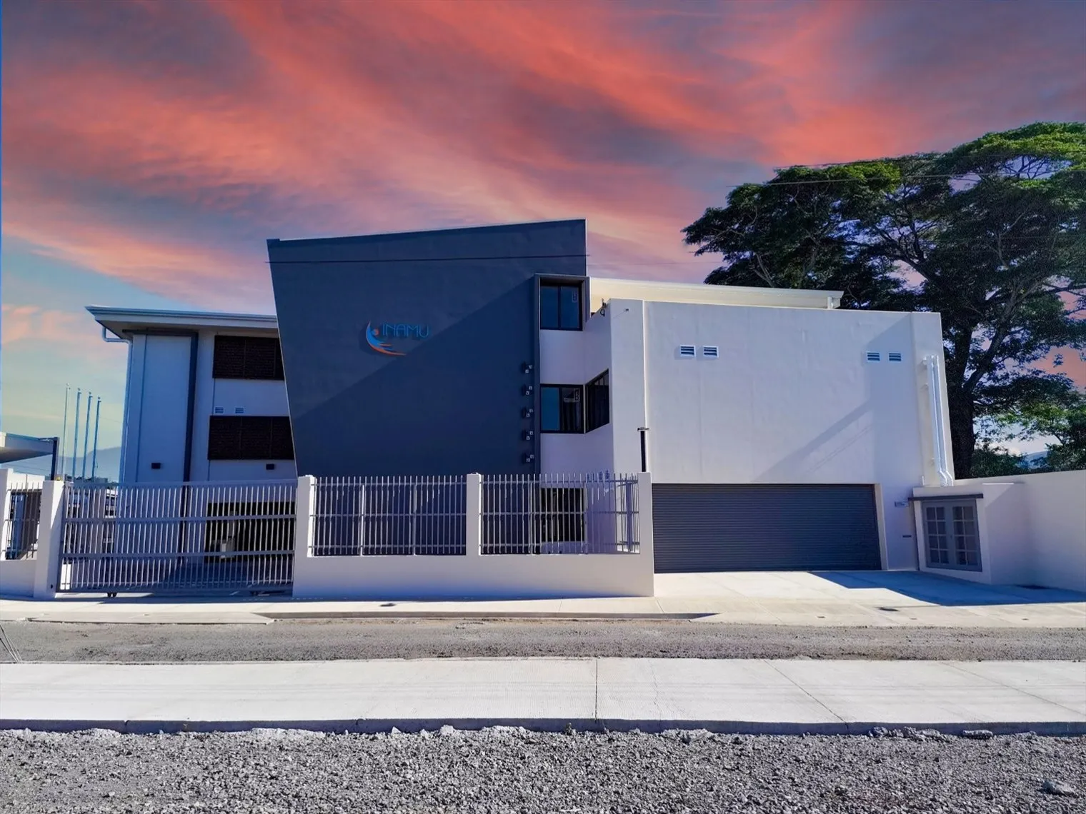 Fachada de la sede del INAMU en Pacífico Central al atardecer, con volumen gris oscuro y portón de acceso